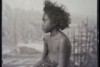 An Aboriginal child sits on a stool in a studio waiting to have his portrait photographed