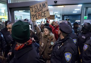 Protesters are surrounded by police officers and travelers as they pass through an exit of Terminal 4 at John F. Kennedy International Airport in New York - President Donald Trump signed an executive order suspending all immigration from countries with terrorism concerns for 90 days.