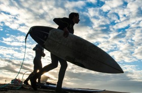 Scattered clouds dot the sky at sunrise as surfers make their way to the water south of the Huntington Beach Pier, a day ...