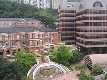 3-storey red brick building with gabled roof adjacent to 7-storey modern building with flat roof.