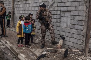 In this Sunday, Dec. 18, 2016 photo, Iraqi children look at the body of a half-buried Islamic State militant while talking to an Iraqi soldier in the al-Barid district in Mosul, Iraq.