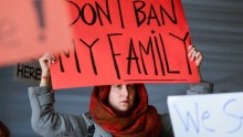 A woman holds a red sign reading don't ban my family