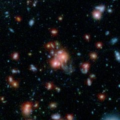 File - A massive cluster of galaxies, called SpARCS1049+56, can be seen in this multi-wavelength view from NASA's Hubble and Spitzer space telescopes.