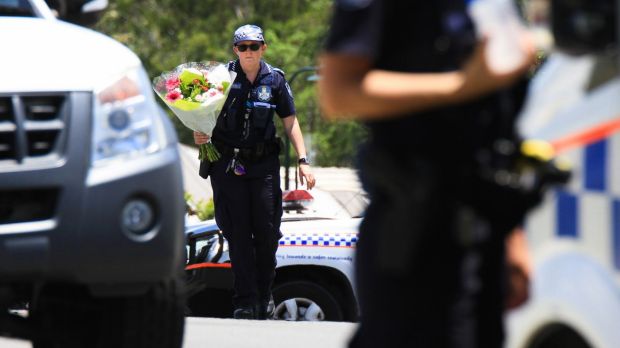 A police officer takes flowers delivered by a neighbour to the scene.