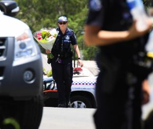 A police officer takes flowers delivered by a neighbour to the scene where Ms Bradford and her estranged husband's ...