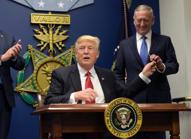 President Donald Trump hands Defense Secretary James Mattis a pen after he signed an executive action on rebuilding the ...