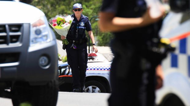 A police officer takes flowers delivered by a neighbour to the scene where Ms Bradford and her estranged husband's ...