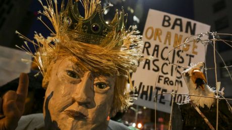 A demonstrator wearing a mask in the likeness of US President Donald Trump protests against his executive order in Los ...