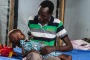 Nyajime Guet, 4, is held by her father Michael as he sits on a bed at a UNICEF-supported clinic.
