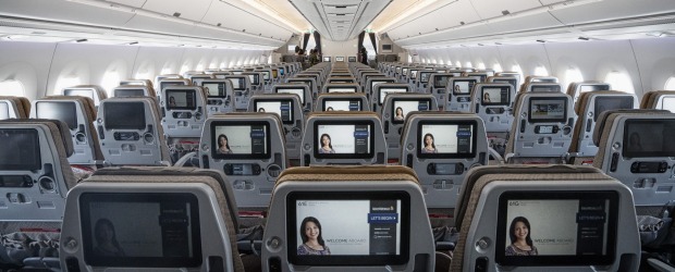 Entertainment monitors sit on the back of passenger seats in the economy class cabin of an Airbus SE A350 aircraft, ...