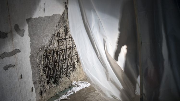 The shadow of a worker is seen repairing a crumbling wall that has been the result of leaking water.