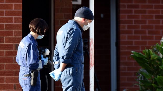 Forensics police walk past blood found on a pole outside units in St Albans.