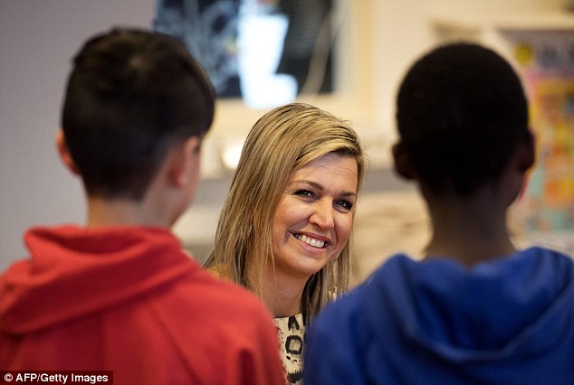 The mother-of-three smiles as she crouches down to talk to young students at the school 