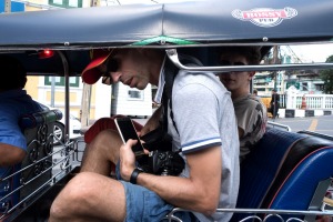 Two male passengers and a driver sit in a tuk-tuk in Bangkok, Thailand.