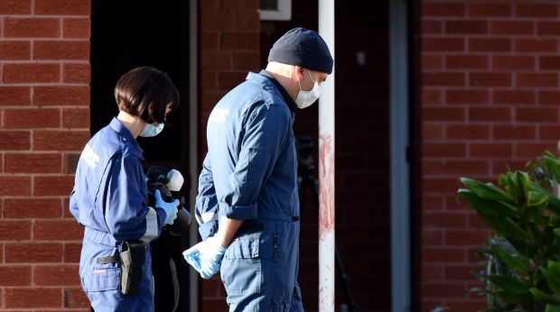 Forensics police walk past blood found on a pole outside units in St Albans.