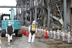 In this Nov. 12, 2014 file photo, workers wearing protective gears stand outside Fukushima Dai-ichi nuclear power plant's reactor in Okuma, Fukushima prefecture, northeastern Japan. As Japan resumed generating nuclear power Tuesday, Aug. 11, 2015, restarting 1 reactor in the south, the destroyed Fukushima Dai-ichi plant remains a highly radioactive site, more than four years after an earthquake and tsunami triggered meltdowns in three of its six reactors.