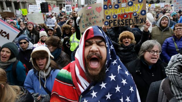 Izzy Berdan, centre wears a US flag as he chants slogans with other demonstrators during a rally against President ...