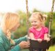 Pretty toddler girl on swing with her mom. She has pigtails and her mom has a braid. They are both blond.