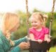 Pretty toddler girl on swing with her mom. She has pigtails and her mom has a braid. They are both blond.
