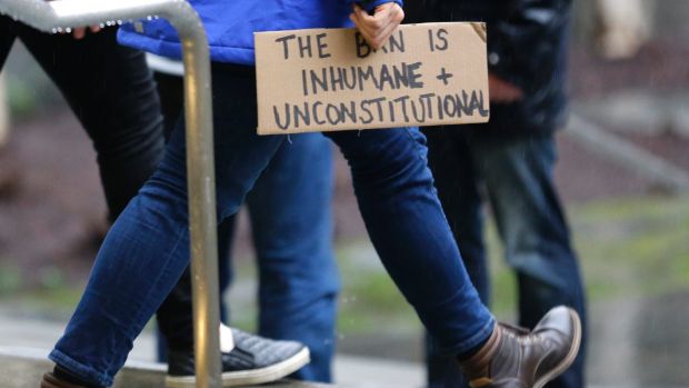 A person walks away from the federal courthouse in Seattle carrying a sign that reads "The Ban is Inhumane and ...