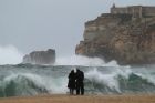 A couple watch the waves breaking in Nazare, Portugal.