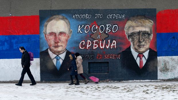 People walk by Serb nationalist graffiti depicting Russian President Vladimir Putin and US President Donald Trump in ...