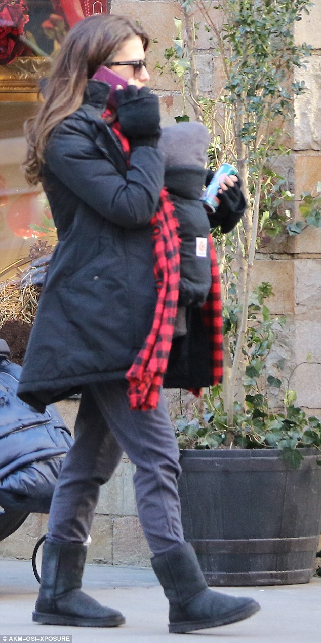 Call waiting: Hilaria sauntered along in front, in a black coat, checked red scarf and back gloves, also taking a call, with their newborn strapped into a papoose on her front