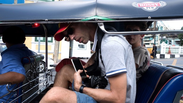 Two male passengers and a driver sit in a tuk-tuk in Bangkok, Thailand.