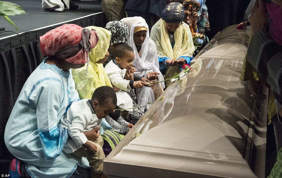 Family members gather around the casket of one of the victims during the ceremony and place roses on the coffin