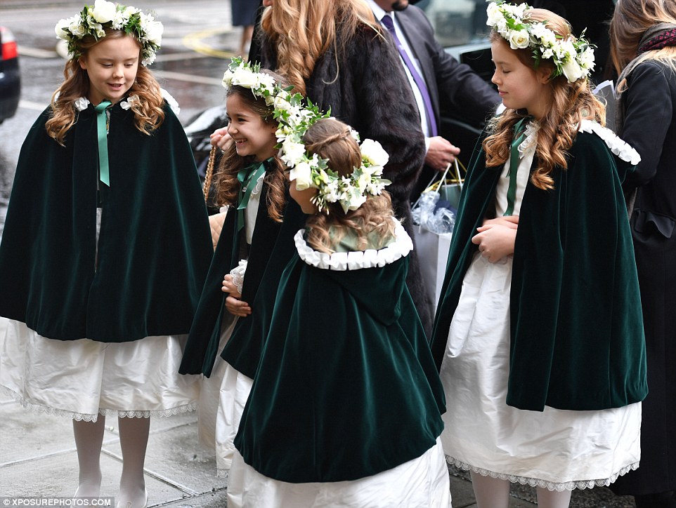 The excited flower girls couldn't contain their joy as they giggled and huddled together on the pavement in their green velvet capes 