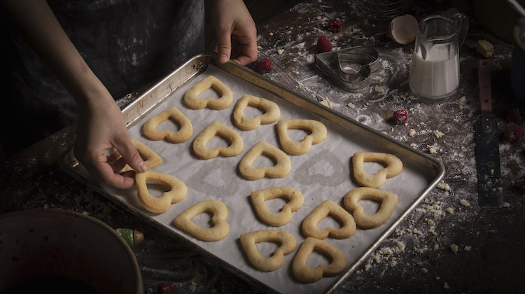 Valentine's Day baking, woman arranging heart shaped biscuits on a baking tray.