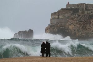 A couple watch the waves breaking in Nazare, Portugal.
