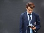 boy in school uniform with headphones looking at his device