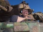 A man wearing a floppy felt hat over earphones and a headset in the cabin of a tank