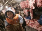 A man shouldering a basket with his grandson inside buys meat at a food market in China