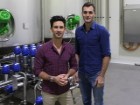 Luke and Matt stand before a series of large stainless steel tanks in an otherwise sterile room