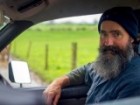 A dairy farmer sitting in a car on his farm wearing a blue beanie