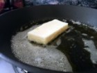 a small off-white rectangle sits in a pool of butter in a black frying pan