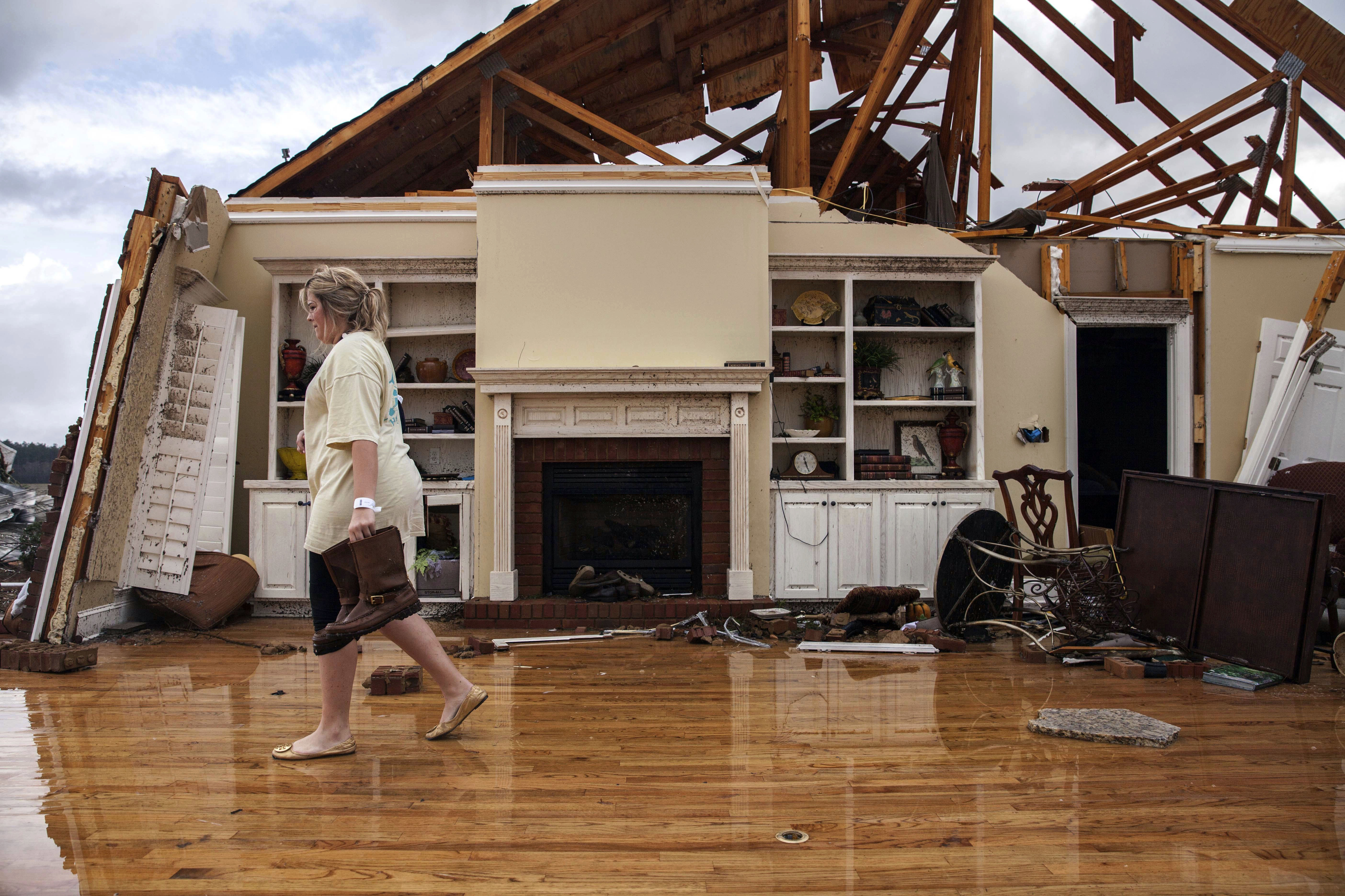 Jenny Bullard carries a pair of boots from her home that was damaged by a tornado, Sunday, Jan. 22, 2017, in Adel, Ga. Georgia Gov. Nathan Deal declared a state of emergency in several counties, including Cook, that have suffered deaths, injuries and severe damage from weekend storms. (AP Photo/Branden Camp)