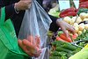A shopper puts produce into a plastic bag while carrying a reusable bag over their other arm, June 12 2009