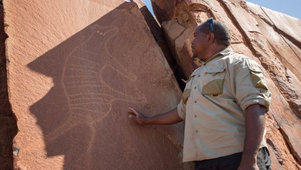 Senior cultural ranger at Murujuga National Park, Dallas Fredericks, stands next to a rock carving of a thylacine ...