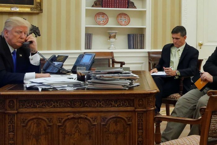 US President Donald Trump seated at his desk with Michael Flynn and Steve Bannon.