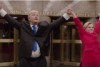 Alec Baldwin and Kate McKinnon stand holding their hands in the air at the entrance to the NBC studio building