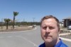 Middle aged man stands looking at camera, with playground, blue sky in background