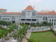 Large white building with a red roof, with a palm-lined path leading up to the main entrance