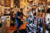 A man in a black Elvis Presley shirt dusting off a shelf of Elvis memorabilia. 