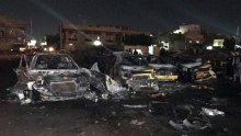 Civilians gather at the site of a car bomb in a used car dealer's parking lot.