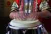 Man wearing a colourful shirt tapping a conga drum. 