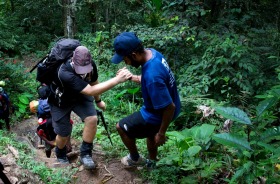 A local porter helps a trekker up a steep section of the Kokoda Track, just after Deniki.