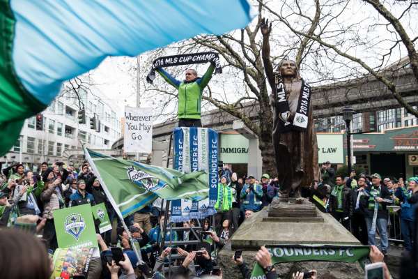 Sounders midfielder Osvaldo Alonso holds up an MLS cup champions scarf next to the statue of Chief Seattle during a march celebrating their recent championship, on Tuesday, Dec. 13, 2016.